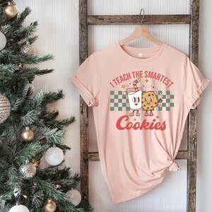 May include: A pink t-shirt with the text "I teach the smartest cookies" in a retro font. A cartoon milk carton and cookie are holding hands.