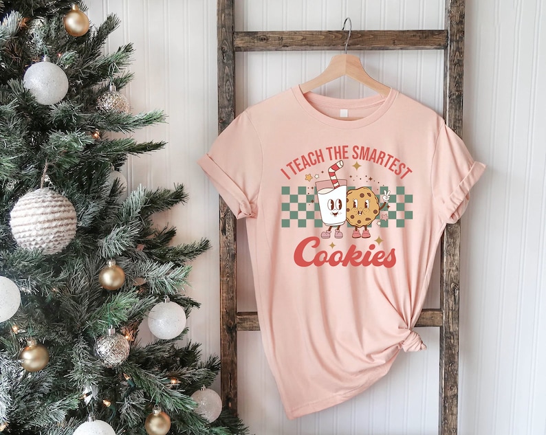 May include: A pink t-shirt with the text "I teach the smartest cookies" in a retro font. A cartoon milk carton and cookie are holding hands.
