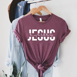 Pu&ograve; includere: Una maglietta color granata con testo bianco che dice "JESUS the way the truth the life".