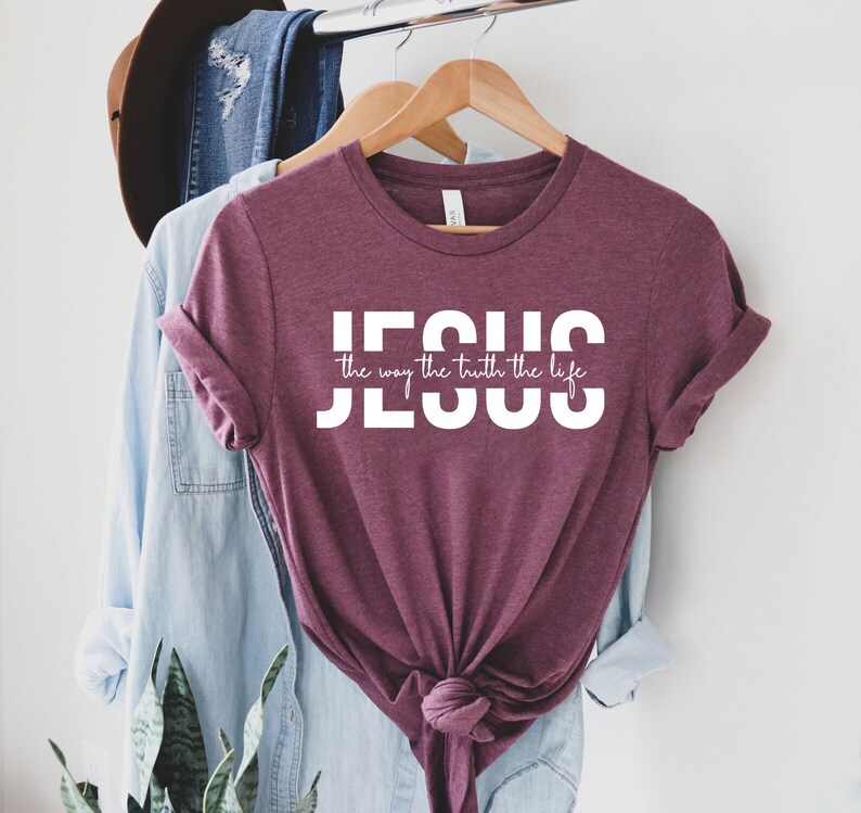 Pu&ograve; includere: Una maglietta color granata con testo bianco che dice "JESUS the way the truth the life".