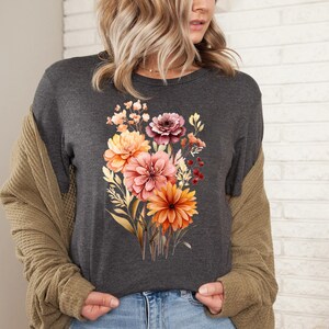 May include: A dark gray t-shirt with a floral print featuring a bouquet of orange, pink, and red flowers. The flowers are surrounded by green leaves and stems.
