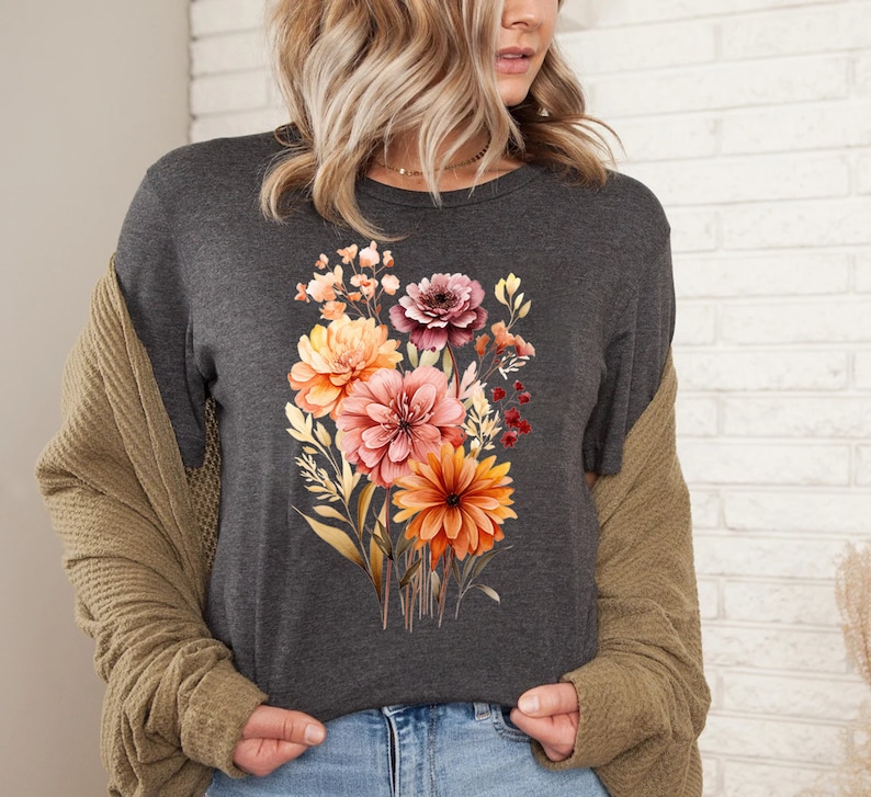 May include: A dark gray t-shirt with a floral print featuring a bouquet of orange, pink, and red flowers. The flowers are surrounded by green leaves and stems.