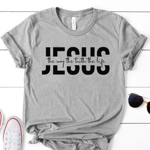 Pu&ograve; includere: Maglietta grigia con testo nero che dice "JESUS the way the truth the life"
