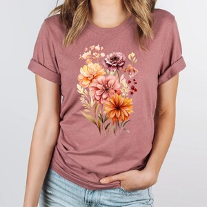 May include: A mauve t-shirt with a floral print featuring a bouquet of orange, yellow, and pink flowers.