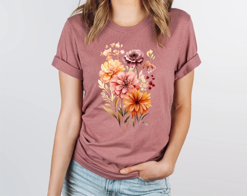 May include: A mauve t-shirt with a floral print featuring a bouquet of orange, yellow, and pink flowers.