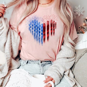 Pu&ograve; includere: T-shirt rosa chiaro con un disegno a forma di cuore con i colori della bandiera americana. Il cuore &egrave; composto da stelle blu e strisce rosse e bianche. La maglietta &egrave; in materiale morbido.