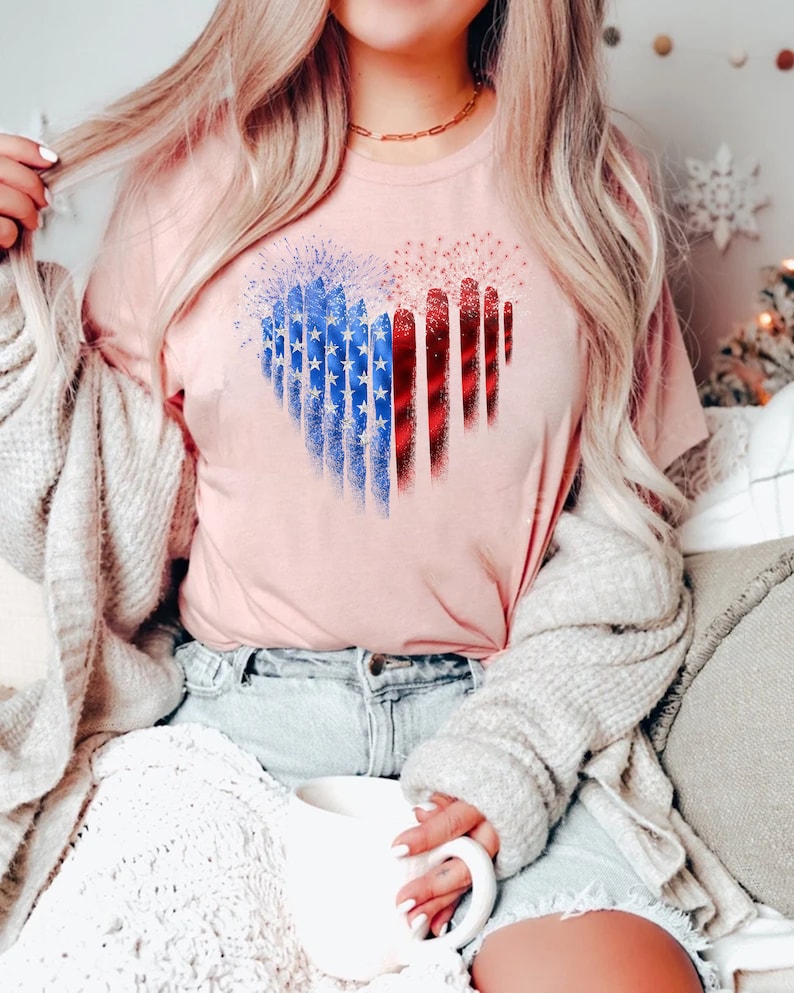 Pu&ograve; includere: T-shirt rosa chiaro con un disegno a forma di cuore con i colori della bandiera americana. Il cuore &egrave; composto da stelle blu e strisce rosse e bianche. La maglietta &egrave; in materiale morbido.