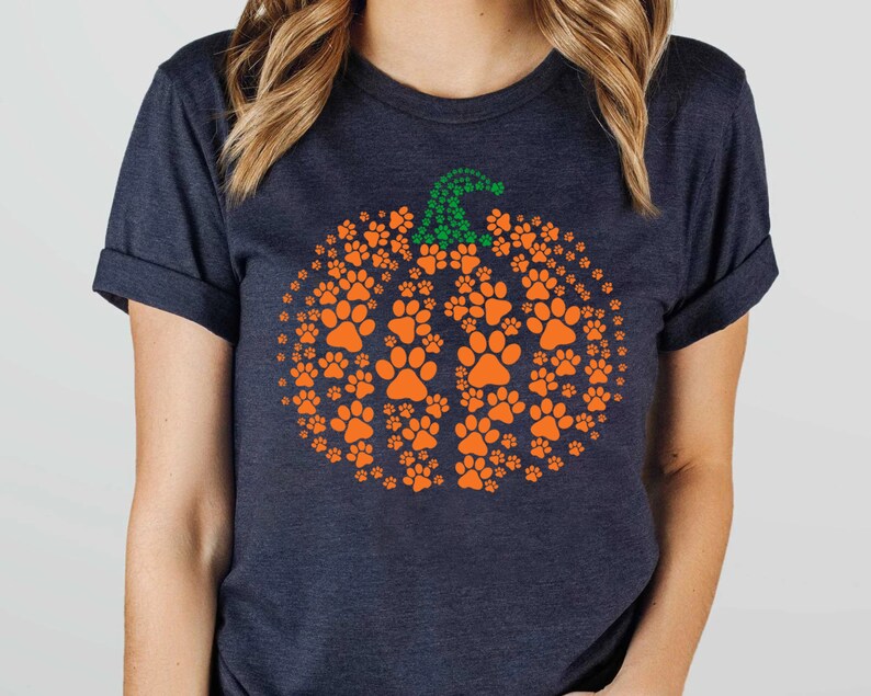 Peut inclure: T-shirt bleu marine fonc&eacute; avec un motif de citrouille orange compos&eacute; d'empreintes de pattes. La citrouille a une tige verte faite de petites empreintes de pattes. Un design amusant et festif pour les amoureux des animaux.