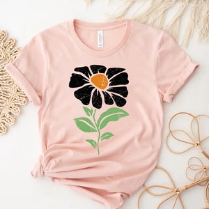 May include: A pink t-shirt with a black and green flower graphic. The flower has a yellow center.