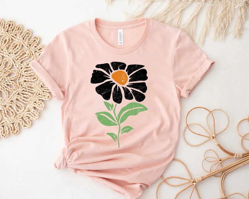 May include: A pink t-shirt with a black and green flower graphic. The flower has a yellow center.