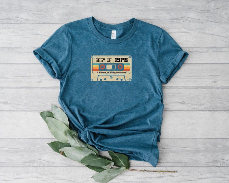 May include: A teal blue t-shirt featuring a vintage cassette tape graphic. The tape has the text "Best of 1976" and "18 Years of Being Awesome".