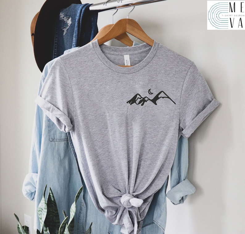 K&ouml;nnte beinhalten: Ein hellgraues T-Shirt mit einem schwarzen Bergpanorama und einem Halbmond-Motiv auf der Vorderseite.