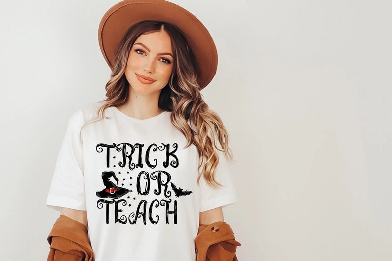 Puede incluir: Camiseta blanca con la frase "TRICK OR TEACH" en letras negras. El dise&ntilde;o incluye un sombrero de bruja y un murci&eacute;lago. Ideal para Halloween o para profesores.