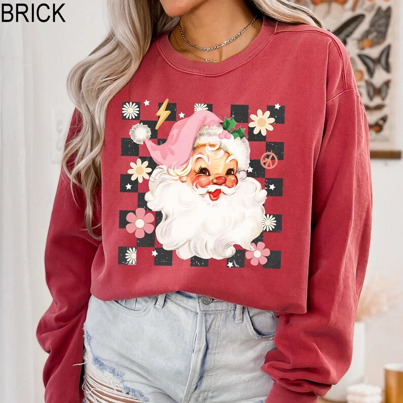 May include: Brick-colored sweatshirt featuring a retro Santa Claus graphic. The Santa design includes a pink hat, white beard, and is surrounded by flowers and a checkered pattern. The word "BRICK" is printed at the top.