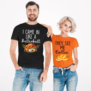 Puede incluir: Dos camisetas con dise&ntilde;os de Acci&oacute;n de Gracias. La camiseta negra dice "I came in like a Butterball" con un gr&aacute;fico de un pavo de Acci&oacute;n de Gracias y guarniciones. La camiseta naranja dice "They see me rollin'" con un gr&aacute;fico de panecillos.