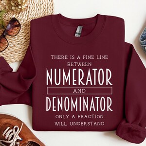 May include: Burgundy sweatshirt with white text that reads "There is a fine line between numerator and denominator. Only a fraction will understand."