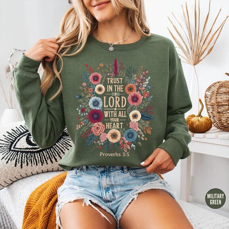 Peut inclure: Sweat-shirt vert militaire avec un motif floral et le texte "Trust in the Lord with all your heart" et "Proverbes 3:5". Le motif floral comprend des fleurs roses, bleues et jaunes.