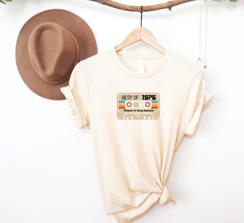 May include: A beige t-shirt featuring a vintage cassette tape graphic that reads "Best of 1976" and "45 Years of Being Awesome".