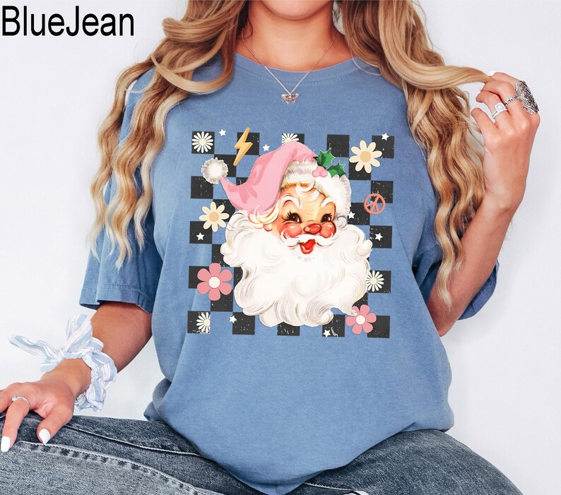 May include: Blue t-shirt with a Santa Claus graphic. The Santa Claus illustration features a pink hat, white beard, and a checkerboard background with flowers and a peace sign. The text "BlueJean" is in the upper left corner.