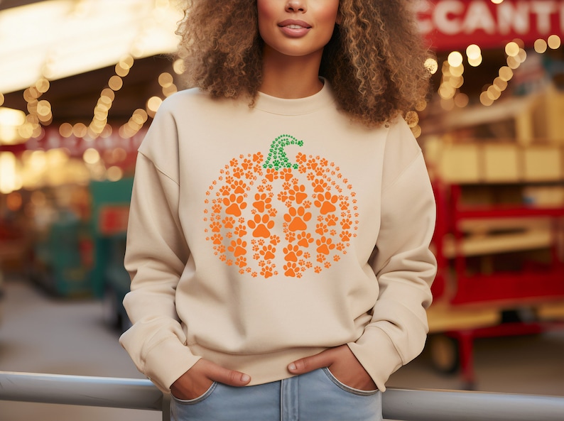 Peut inclure: Sweat-shirt beige avec un motif citrouille en empreintes de pattes orange et une tige verte. La citrouille est compos&eacute;e de nombreuses empreintes de pattes orange. Un haut d&eacute;contract&eacute; pour l'automne et Halloween.