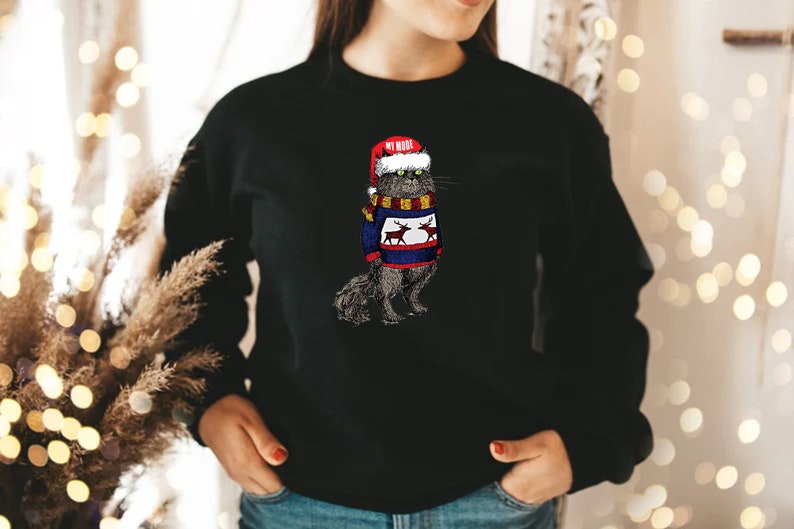 K&ouml;nnte beinhalten: Ein schwarzer Pullover mit einem Aufdruck eines Katers, der einen Weihnachtsmann-Hut und einen Weihnachtspullover mit Rentieren tr&auml;gt. Der Text "My Mood" steht auf dem Hut.