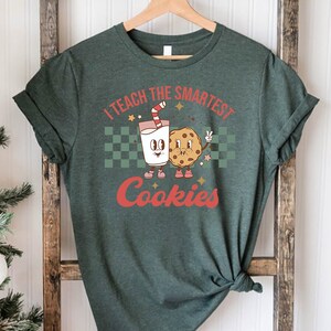 May include: A green t-shirt with the text "I teach the smartest cookies" in white and red lettering. A cartoon milk carton and cookie are holding hands.