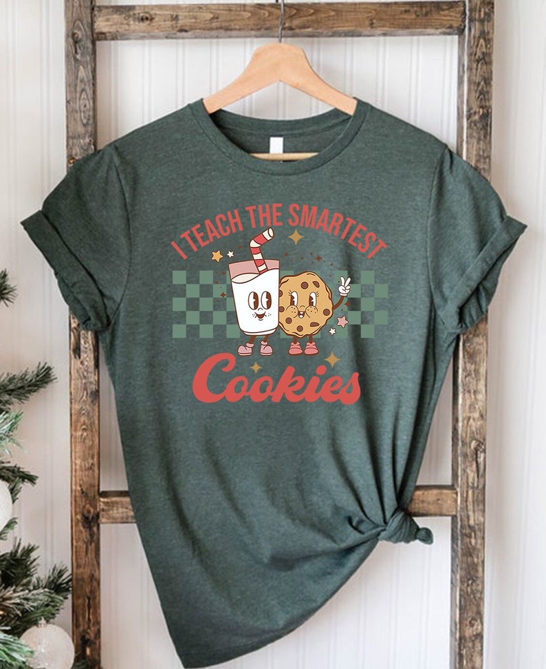 May include: A green t-shirt with the text "I teach the smartest cookies" in white and red lettering. A cartoon milk carton and cookie are holding hands.