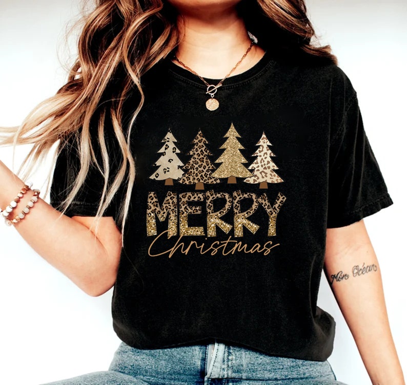 May include: Black t-shirt with a gold glitter "Merry Christmas" graphic featuring three Christmas trees with leopard print and gold glitter accents.