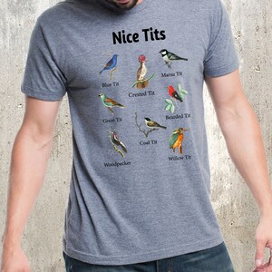 May include: A heather gray t-shirt with a humorous design featuring the text "Nice Tits" and illustrations of different types of birds, each labeled with their common name, such as "Blue Tit", "Crested Tit", and "Willow Tit".