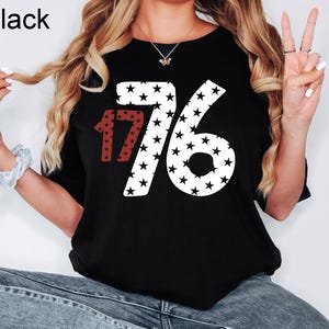 Puede incluir: Camiseta negra con un gr&aacute;fico blanco y rojo del n&uacute;mero 1776 hecho de estrellas.