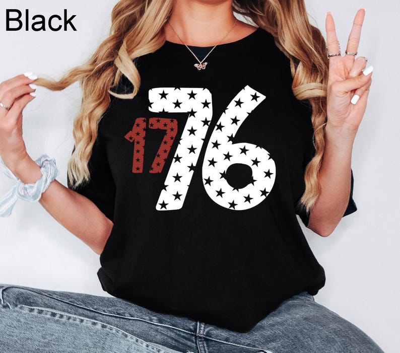 Puede incluir: Camiseta negra con un gr&aacute;fico blanco y rojo del n&uacute;mero 1776 hecho de estrellas.