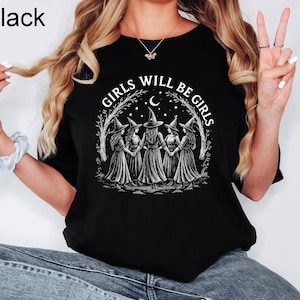 K&ouml;nnte beinhalten: Schwarzes T-Shirt mit dem Text "GIRLS WILL BE GIRLS" in einem kreisf&ouml;rmigen Design. Das Design zeigt f&uuml;nf Figuren in Hexenh&uuml;ten und Kleidern, die sich unter einem Halbmond und Sternen an den H&auml;nden halten. Das Wort "Black" befindet sich in der oberen linken Ecke.