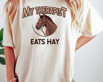 May include: A white t-shirt with the text "My Therapist Eats Hay" and a brown horse illustration.
