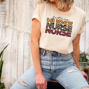 May include: A cream colored t-shirt with the text "future nurse" in a layered design with leopard print and orange and pink accents.