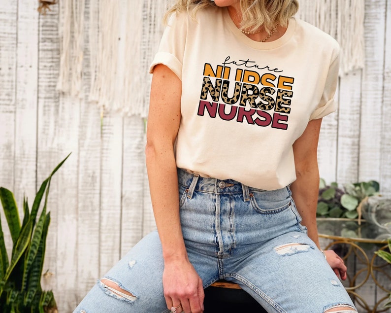 May include: A cream colored t-shirt with the text "future nurse" in a layered design with leopard print and orange and pink accents.