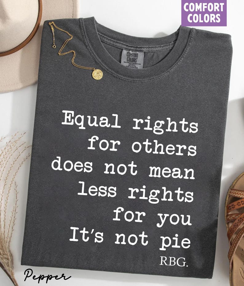 May include: Dark gray Comfort Colors t-shirt with the text "Equal rights for others does not mean less rights for you. It's not pie. RBG." A gold necklace and a tan hat are visible.