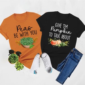 Puede incluir: Dos camisetas con dise&ntilde;os de oto&ntilde;o. La camiseta naranja dice "Peas Be With You" y presenta un taz&oacute;n de guisantes. La camiseta negra dice "Give 'Em Pumpkin To Talk About" y presenta tres calabazas.