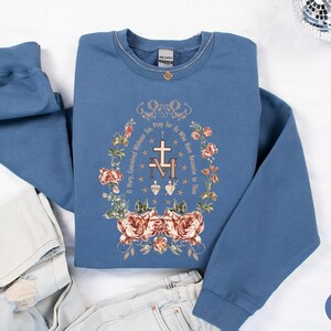 Puede incluir: Sudadera azul &iacute;ndigo con un dise&ntilde;o floral y el texto "Oh Mar&iacute;a, concebida sin pecado, ruega por nosotros que recurrimos a ti".