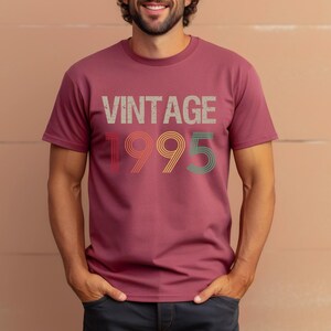 May include: A maroon t-shirt with the text "Vintage 1995" in a retro font with multi-colored outlines.