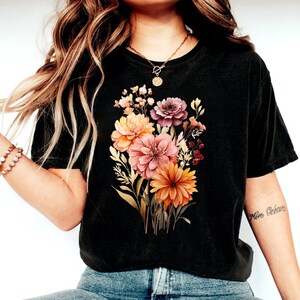 May include: A black cropped t-shirt with a floral print featuring a bouquet of orange, pink, and purple flowers. The flowers are surrounded by green leaves and stems.