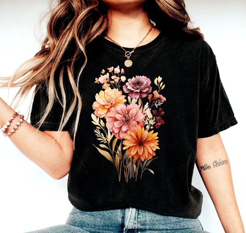 May include: A black cropped t-shirt with a floral print featuring a bouquet of orange, pink, and purple flowers. The flowers are surrounded by green leaves and stems.