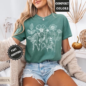 May include: Light green t-shirt with a white floral design. The shirt has short sleeves and a crew neck. The words "COMFORT COLORS" are in a black box in the upper right corner. The words "FAST SHIPPING" are in a black circle.