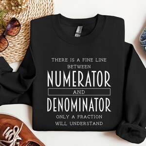 May include: Black sweatshirt with white text that reads "There is a fine line between numerator and denominator. Only a fraction will understand."