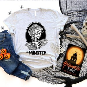 May include: A gray t-shirt with a black and white illustration of a skeleton with flowers in its hair. The text "#MOMSTER" is printed below the illustration.