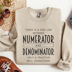May include: A beige sweatshirt with the text "There is a fine line between numerator and denominator. Only a fraction will understand."