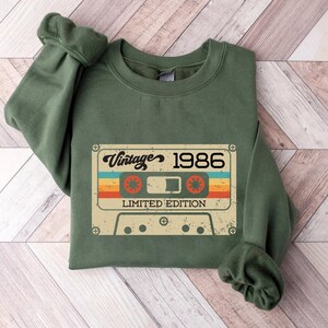 May include: Green sweatshirt featuring a vintage cassette tape graphic that reads "Vintage 1986 Limited Edition".
