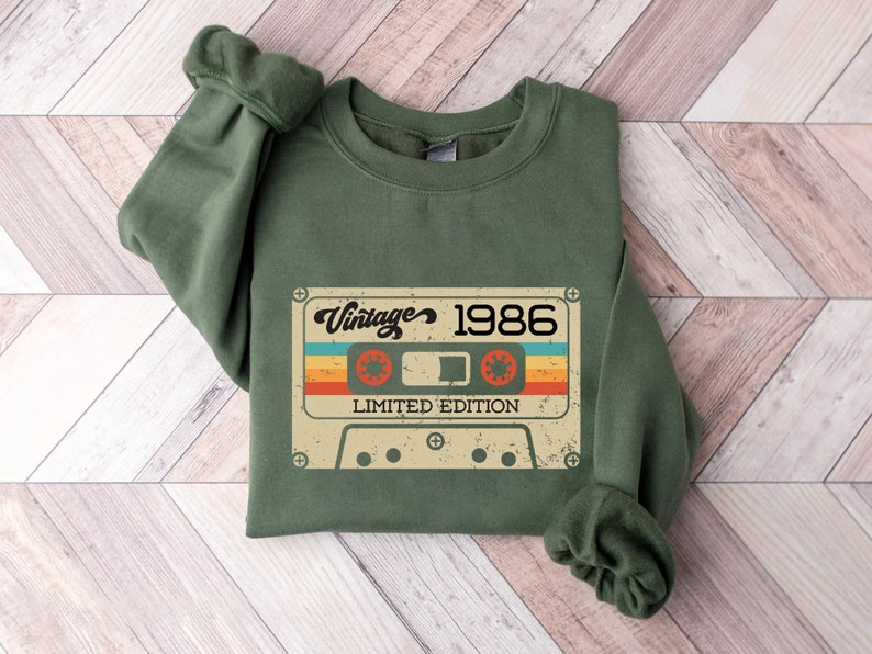 May include: Green sweatshirt featuring a vintage cassette tape graphic that reads "Vintage 1986 Limited Edition".