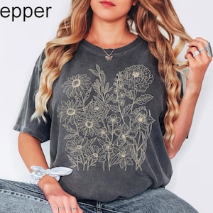 K&ouml;nnte beinhalten: Dunkelgraues T-Shirt mit beigem Blumendesign. Das Shirt hat einen Rundhalsausschnitt und kurze &Auml;rmel. Das Wort "Pepper" befindet sich in der oberen linken Ecke. Das Model tr&auml;gt eine blaue Jeans.