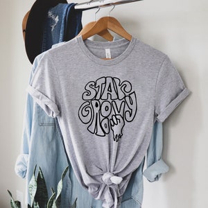 May include: A grey t-shirt with a black graphic that says "Stay Groovy" in a retro font.