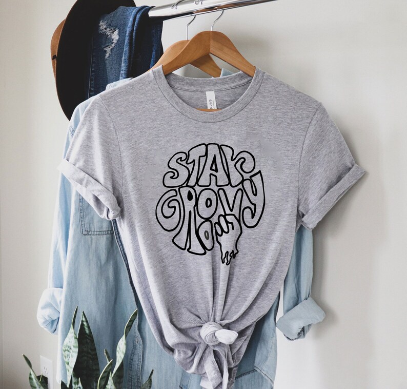 May include: A grey t-shirt with a black graphic that says "Stay Groovy" in a retro font.